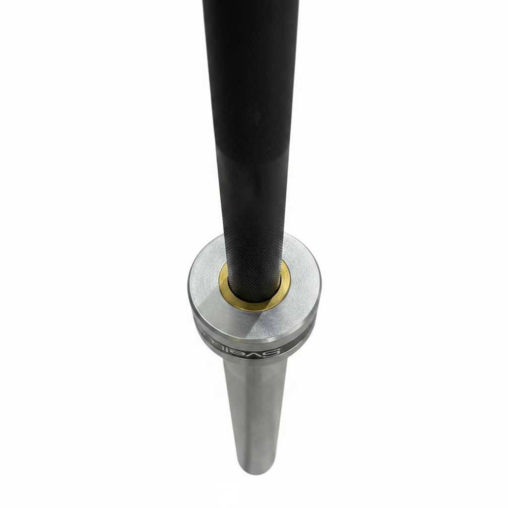 A close-up of a silver and black barbell base with a gold accent ring, set on a dark speckled gym floor.