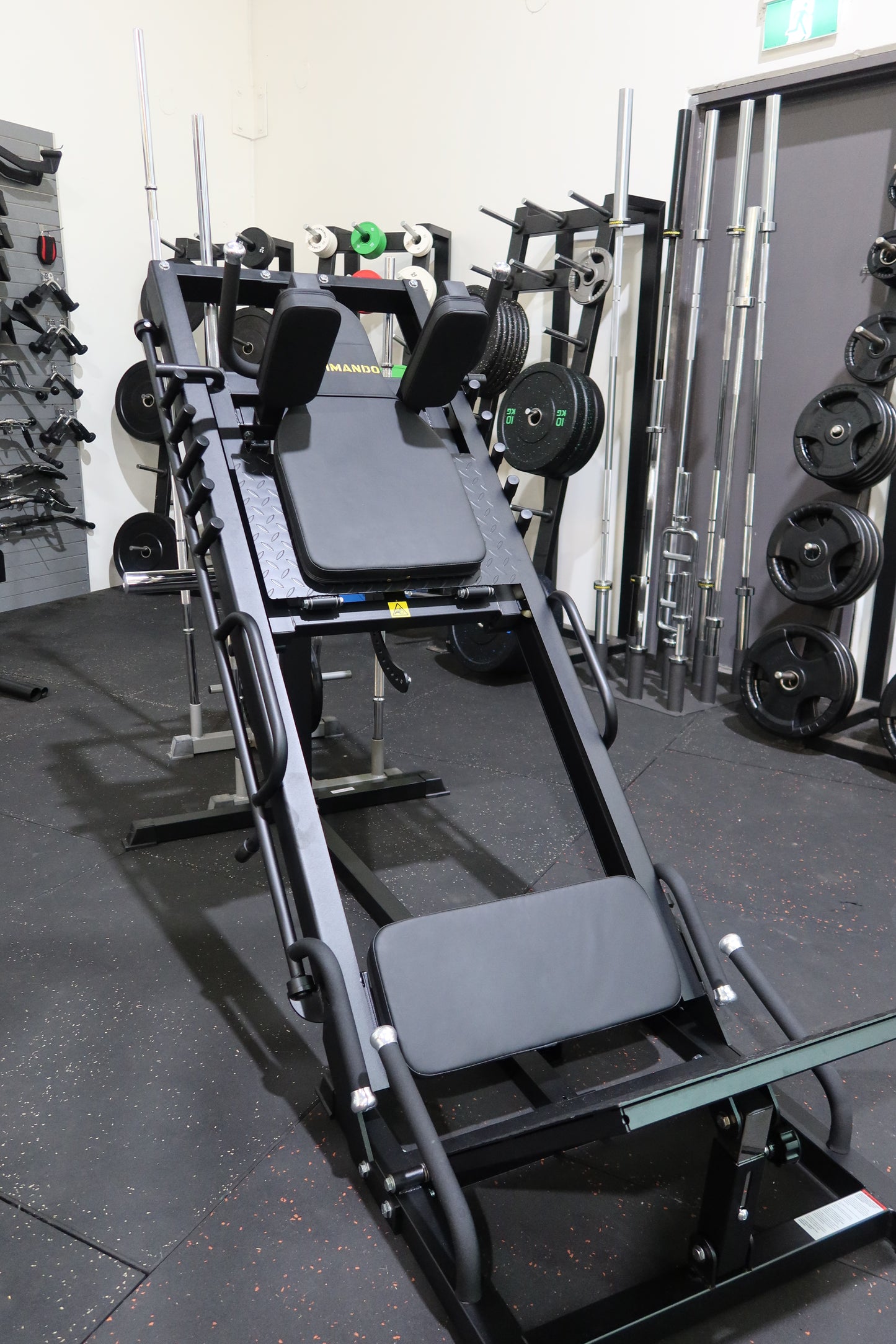 Gym equipment including weight plates and a bench on a black floor.