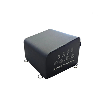 A black GLUTE PLQ BOX fitness accessory with printed exercise diagrams on the front, placed on a light wood floor inside a gym.