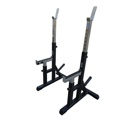 A pair of black and silver AEX power racks with safety arms, positioned on a concrete surface in front of a building with a white garage door.