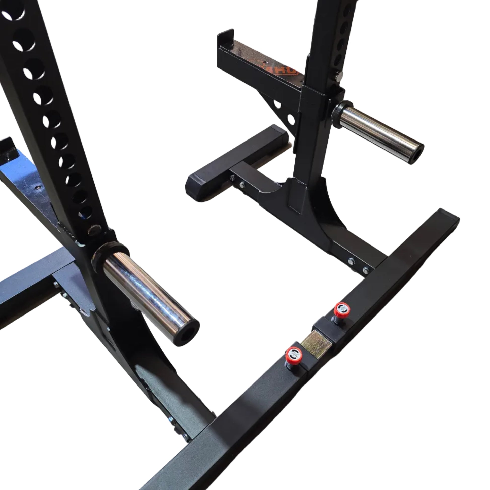 Black steel power rack with a barbell and weight plates, photographed in a warehouse or gym setting on a concrete floor with cardboard boxes in the background.