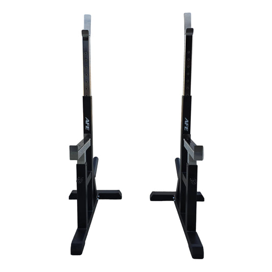 Two black adjustable squat racks with white measurement markings, positioned side-by-side on a concrete floor in front of a white garage door.