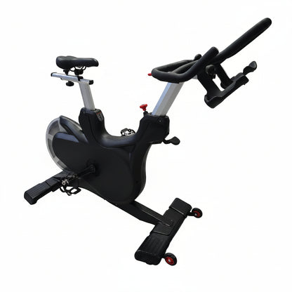 A black and silver indoor stationary exercise bike with a padded seat and adjustable handlebars, photographed on a light wood floor in front of a draped white fabric backdrop.